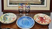 Two plastic polka dot wine glasses and six decorative plates arranged on table, showing variety of patterns and colors.