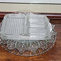 Stacked plates showing three rectangular Pyrex refrigerator plates with divided sections on top of a larger decorative glass plate with a geometric pattern.