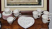 View showing all items including 4 tea cups, 4 coffee cups, 10 saucers, and 1 heart-shaped serving plate on wooden surface.