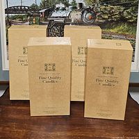 Four unopened beige boxes labeled 'Fine Quality Candles' from Williamsburg brand, displayed on a wooden surface.