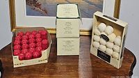 Photo showing three packages of votive candles in red, cream/white, and white colors with visible packaging labels.
