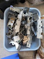 Bin filled with various galvanized metal brackets and hardware pieces, showing multiple shapes and sizes stacked loosely.