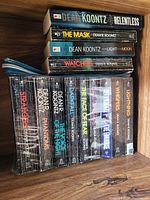 Photo showing a stack of 12 Dean Koontz books placed on a wooden surface, including single titles and a boxed set.