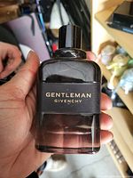 Photo showing front of Gentleman Givenchy cologne bottle with black tinted glass and black branded band label held in hand.