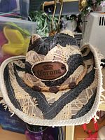 Front angled view of decorative straw hat with Corona Mexico leather patch, black and beige woven pattern, and lace trim