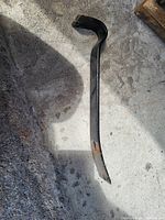 Metal crowbar laying on concrete surface, showing wear and some rust.