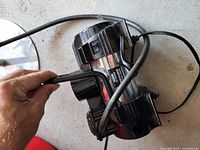 Photo showing the top and side of the black flashlight, highlighting the on/off switch, metallic body, and attached power cord.