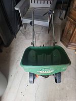 Green Scotts Deluxe fertilizer spreader with metal handle and wheels on concrete floor.