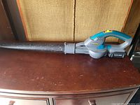 Cordless leaf blower on a wooden surface, with battery attached at the handle base.