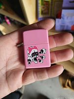 Photo of a small pink lighter held in hand showing front design of skulls and mushroom.