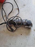 Handheld electric oscillating multi-tool resting on concrete floor, showing the Dremel brand label and power cord.
