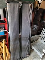 Black folding truck bed cover standing upright among other furniture items.