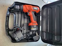 Open case showing Black & Decker orange and black cordless drill with battery attached, charger and cord.