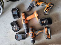 Overhead view of four Ridgid cordless drills/drivers and four Ridgid 18V battery packs on a concrete floor.