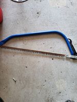 Hand saw with blue curved handle and toothed blade lying on a concrete floor.