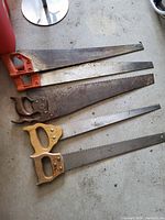 Photo of five hand saws laying parallel on a surface showing various handle types and blade lengths