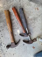 Photo of three used claw hammers on a concrete surface.