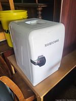 Closed view of the white Mobicool small fridge showing front chrome latch and top handle.