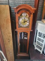 Full view of the wooden stand up grandfather clock showing the detailed clock face with Roman numerals and pendulum visible through the lower glass panel.