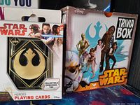Photo showing two boxed Star Wars items: a collectible embossed tin playing cards deck and a trivia box game.
