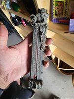 Close-up photograph of an ornate vintage style temperature gauge with a vertical scale and red liquid indicator tube, held in hand