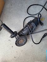 Black & Decker angle grinder laid on floor showing power cord, side handle and disc