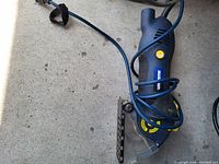 Photo shows a black and blue Mastercraft electric jigsaw with power cord, yellow button, and blade guard on work surface.