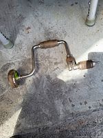 Vintage hand crank drill with wooden handles on concrete floor under sunlight.