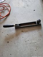 Photo showing the metal handheld rasp on a rough concrete surface with an orange extension cord partially visible in the upper left corner.