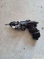 Electric handheld screwdriver with power cord and plug coiled around it, photographed on a light grey surface.