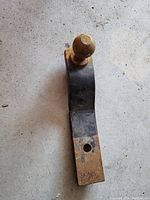 Truck hitch ball mount with rust and one hole for mounting, placed on a concrete floor.