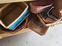 Photo showing seven wicker baskets of various shapes, sizes, and colors placed on a wooden surface and floor, illustrating the lot contents.
