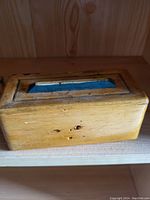 Wooden rectangular box with closed lid showing natural wood grain, some dark spots, and a rectangular inset on the lid.