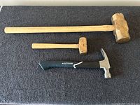 Photo of two wooden-handled sledgehammers and one MasterCraft claw hammer on black surface.