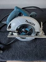 Makita circular saw with visible blade and teal handle on dark surface