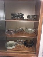 Shelf view of 13 ashtrays including stacked and individual clear glass ashtrays and white ceramic ashtray.
