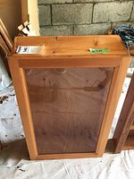 Front view of the handmade wooden cabinet with a glass door showing scratches and natural wood finish in a garage setting.