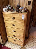 Front view of five-drawer wooden dresser with metal hardware and items on top (not included).