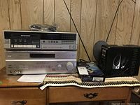 View of Sony control center, Sears Betavision VCR, Roxio VHS to DVD 3 Plus box, and Recoton Navigator speaker system box on a wooden surface.