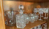 Wide shelf view showing entire glassware set including decanter, pitcher, bowl, and glasses arranged on wood shelf