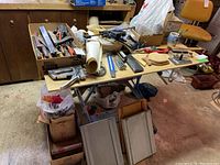 Wide view of workbench with box holding assorted hand tools including files, rasps, pliers, clamps, stapler, and wrecking bar under fluorescent lighting in a basement setting.