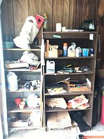 Two wooden shelving units filled with assorted wood blocks, tools, boxes, and hardware items against a wood-paneled wall in a garage setting.