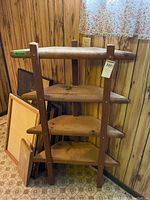 Front view of handmade wood shelf with four wooden shelves and dark vertical supports, against wood-paneled wall.