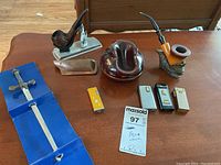 Full lot overview with two pipes, four lighters, two ash canisters, decorative stands, and letter opener in blue case on wooden table.
