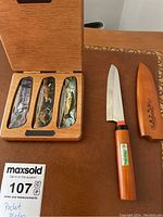 Three pocket knives with wildlife theme handles displayed in fitted wooden case next to fruit knife with wooden sheath.