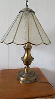 Full view of the table lamp showing solid brass base and textured glass shade with scalloped edges.