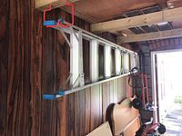 Side view of aluminum step ladder on wooden wall background; ladder laid flat on wall with blue rubber feet visible.