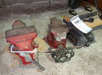 Three red metal vises grouped on floor showing varied sizes and wear