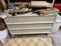 Front view of metal tool chest with three drawers, showing scuffs and paint wear. Items stacked on top obscuring some details.