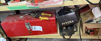 Photo of red metal toolbox along with additional tools on shelf